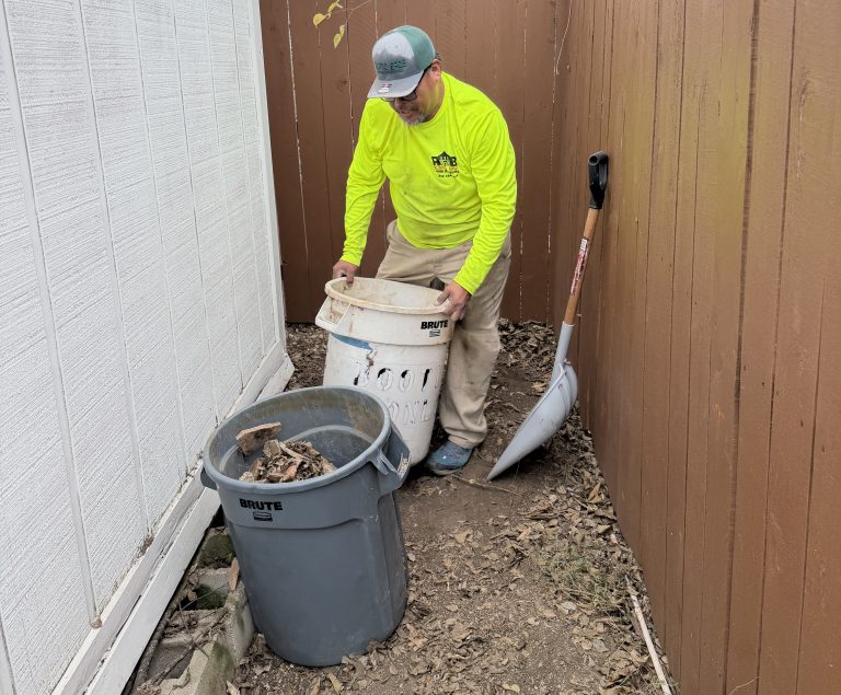 Alamo Bros crew member collecting yard debris beside a fence