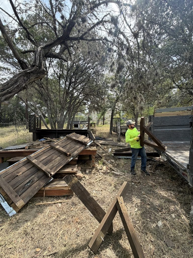 Alamo Bros worker carrying dismantled wooden deck lumber toward a debris trailer