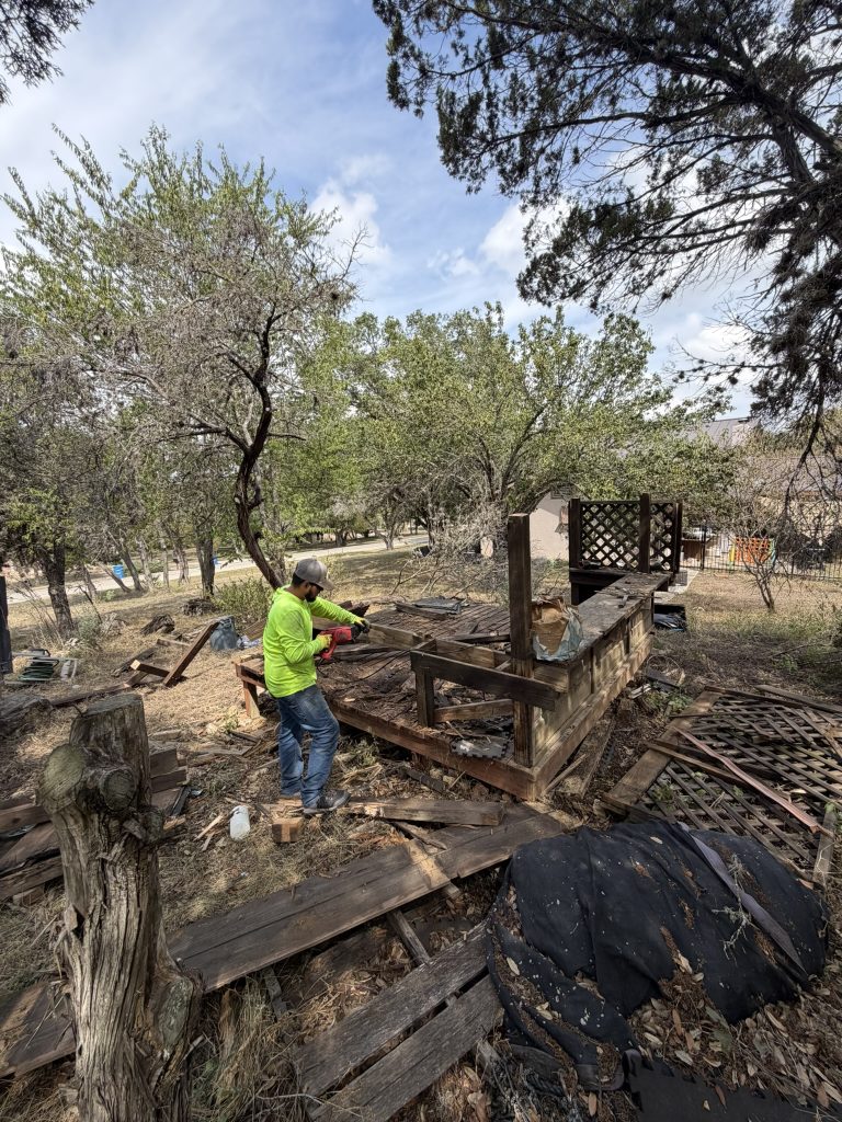 Alamo Bros worker dismantling a wooden deck frame with a power saw
